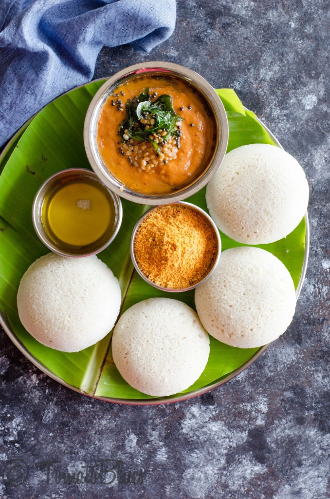 Steamed idlis on banana leaf with sambar, chutney, and podi